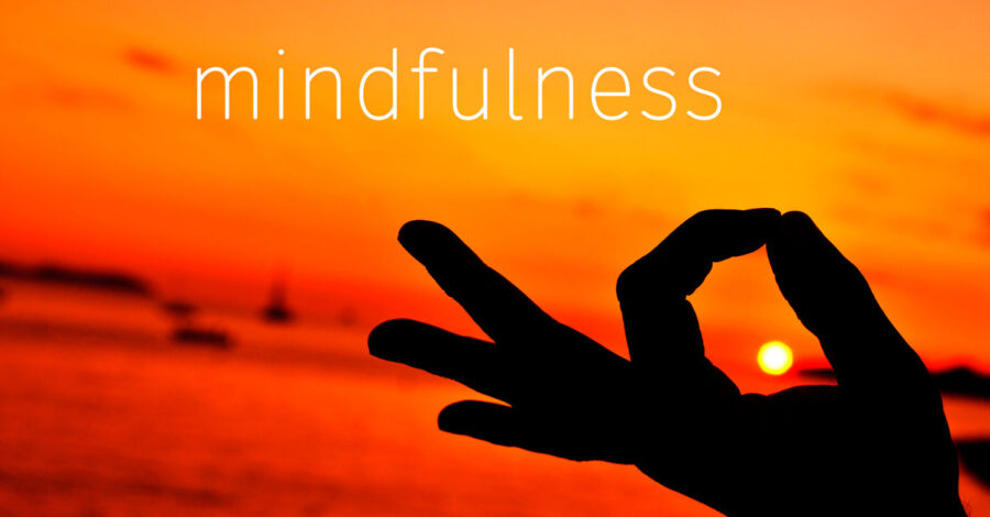 Mindfulness written in orange and yellow sunset sky with a person holding their pointer finger and thumb together as if they were meditating | What is Mindfulness | Breaking Dawn Therapy