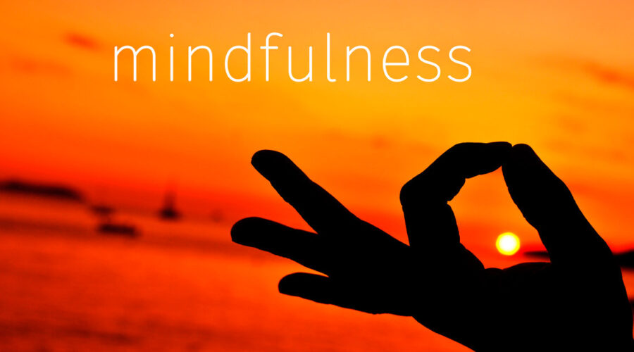 Mindfulness written in orange and yellow sunset sky with a person holding their pointer finger and thumb together as if they were meditating | What is Mindfulness | Breaking Dawn Therapy