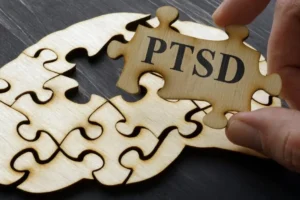 Person Holding A Puzzle Piece That Reads PTSD With Blank Puzzle Pieces In The Background On A Table | How To Heal From PTSD | Breaking Dawn Therapy