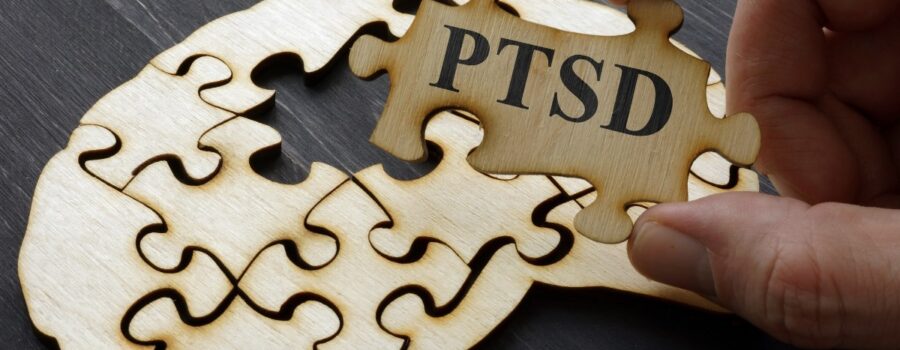 Person Holding A Puzzle Piece That Reads PTSD With Blank Puzzle Pieces In The Background On A Table | How To Heal From PTSD | Breaking Dawn Therapy