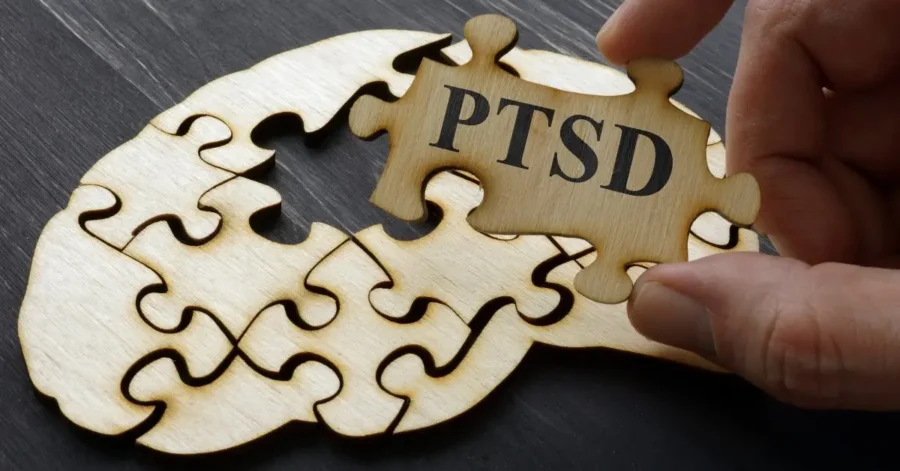 Person Holding A Puzzle Piece That Reads PTSD With Blank Puzzle Pieces In The Background On A Table | How To Heal From PTSD | Breaking Dawn Therapy