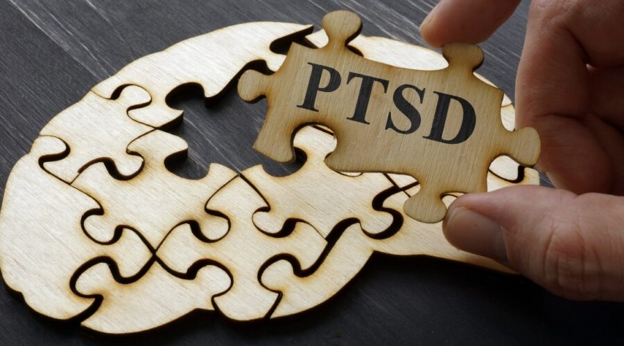Person Holding A Puzzle Piece That Reads PTSD With Blank Puzzle Pieces In The Background On A Table | How To Heal From PTSD | Breaking Dawn Therapy