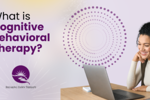 A Younger Woman Sitting At A Table With Earphones in Looking At A Laptop Smiling | What is Cognitive Behavioral Therapy? | Breaking Dawn Therapy
