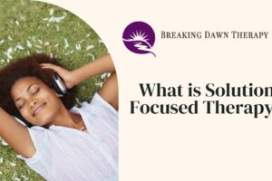 A Woman Laying in the Grass With Headphones on Smiling | What is Solution-Focused Therapy? | Breaking Dawn Therapy
