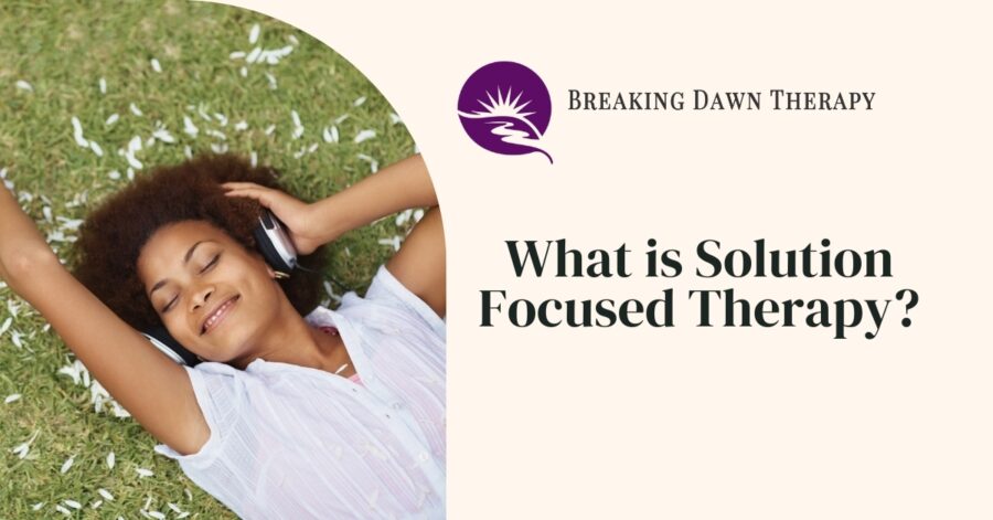 A Woman Laying in the Grass With Headphones on Smiling | What is Solution-Focused Therapy? | Breaking Dawn Therapy