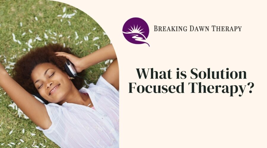 A Woman Laying in the Grass With Headphones on Smiling | What is Solution-Focused Therapy? | Breaking Dawn Therapy